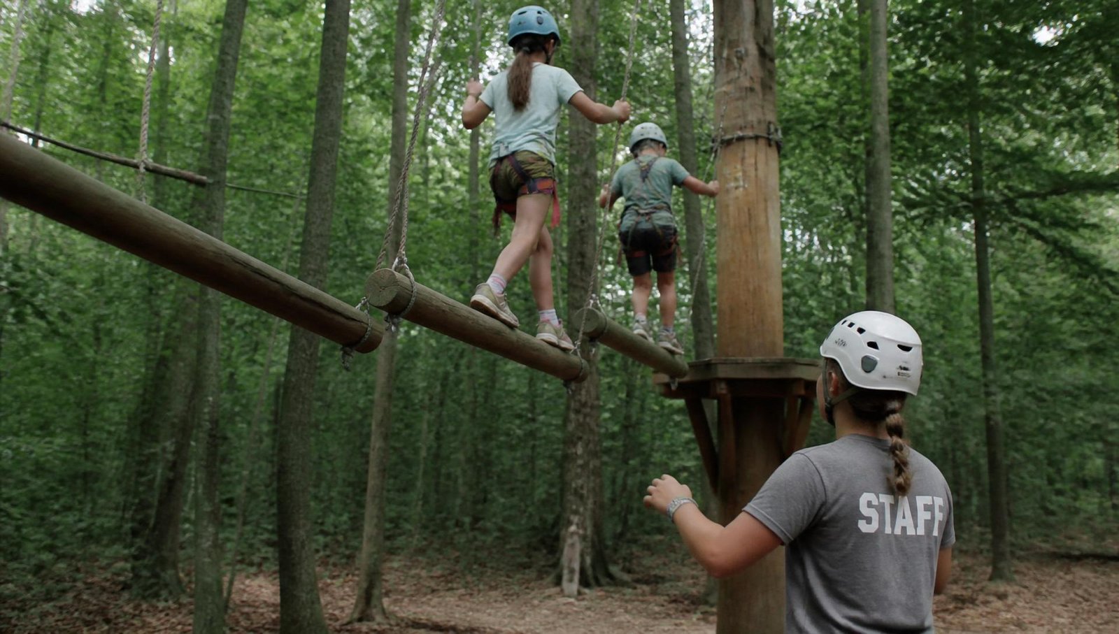 Campers crossing a low ropes course element while a staff member spots them