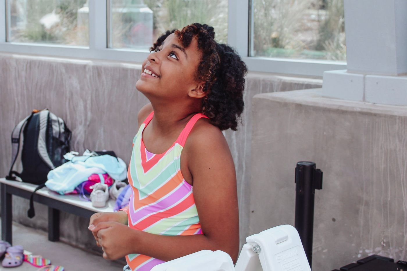 A camper smiling and looking up while sitting on a bench beside her backpack