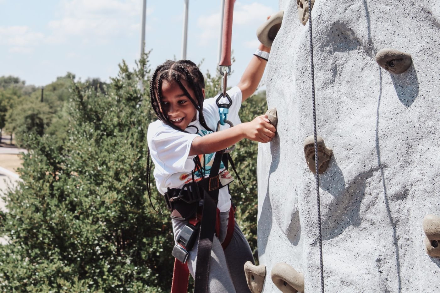A camper in a harness climbing a rock wall outdoors